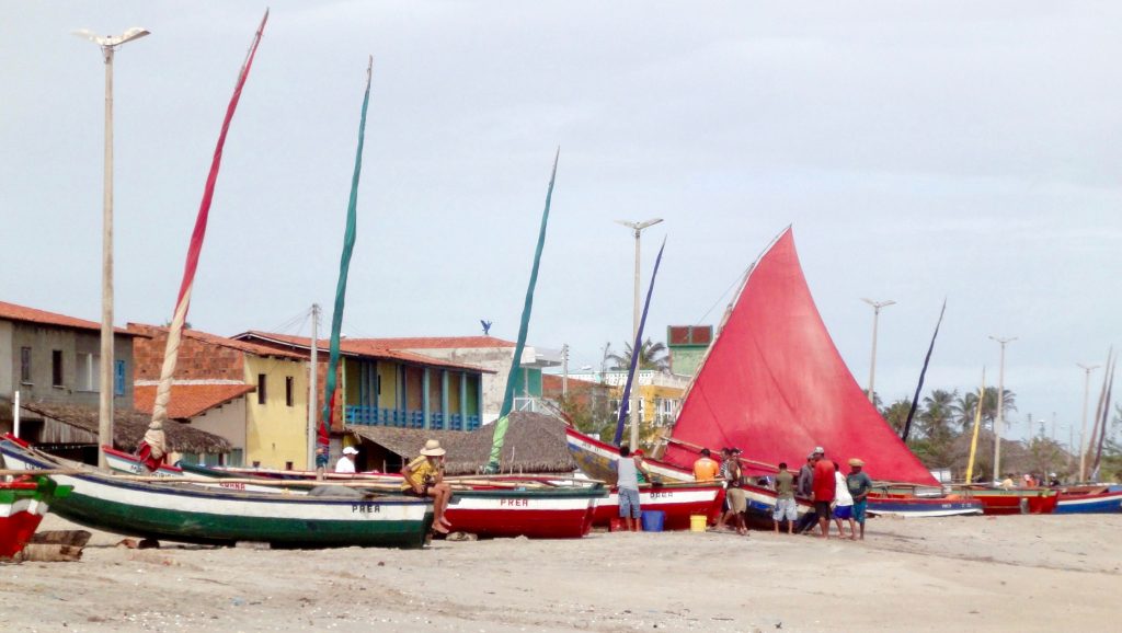 Men gathered around a jangada on the beach in Brazil. 