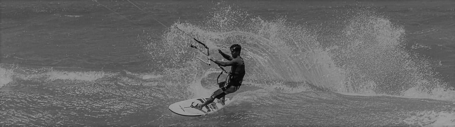 Panoramic, black and white shot of kitesurfer riding wave. ,