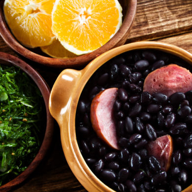Feijoada with a dish of orange slices and kale.